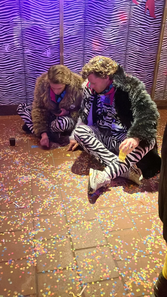 Twee PPEM-leden in bontjassen en zebrapakken tussen de confetti
